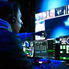 Man with headset with blue-lit monitors and tech gear