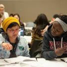 Two students look at notebooks and paper in a crowded classroom at UC Davis. 