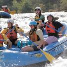 A group of people white-water rafting in a blue inflatable boat.