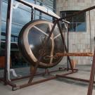 Man holds gong striker, next to Gong sculpture