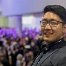 Smiling man with glasses and headphones before a blurred audience