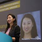 Woman speaks at podium, with her headshot on screen behind her.