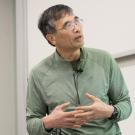Person wearing green shirt and glasses looks up at whiteboard during lecture