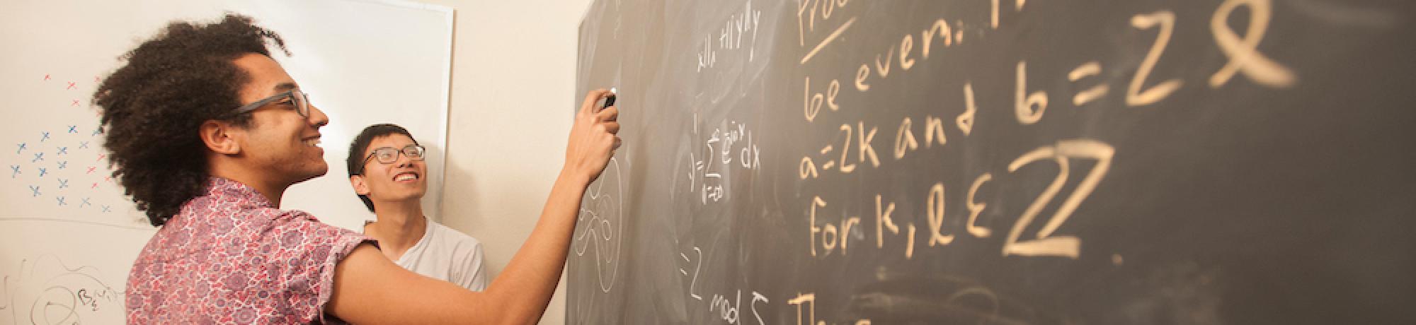 A student does equations at a blackboard.