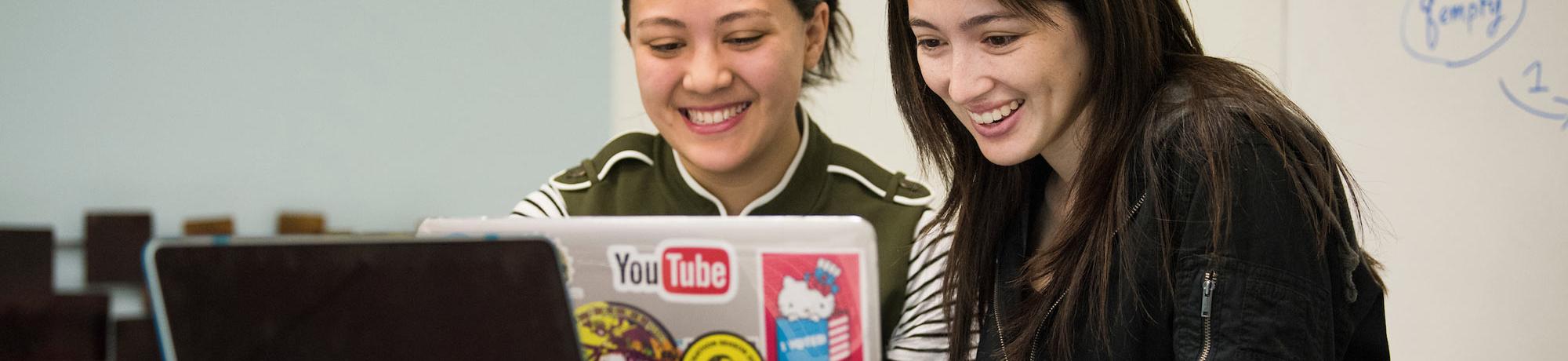 Two female students share a laptop to evaluate their work.