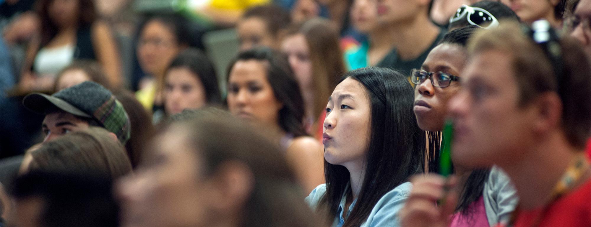 closeup of three students in a crowd of students attending a lecture