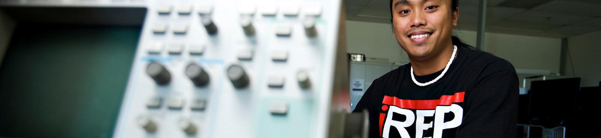 A male student poses next to some engineering lab equipment