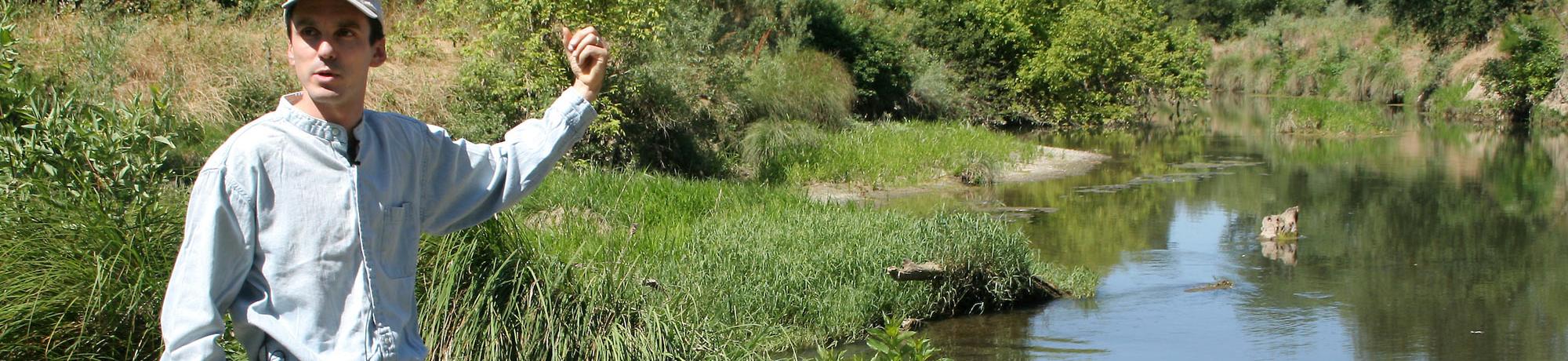 A UC Davis researcher points at a wetlands areas behind him