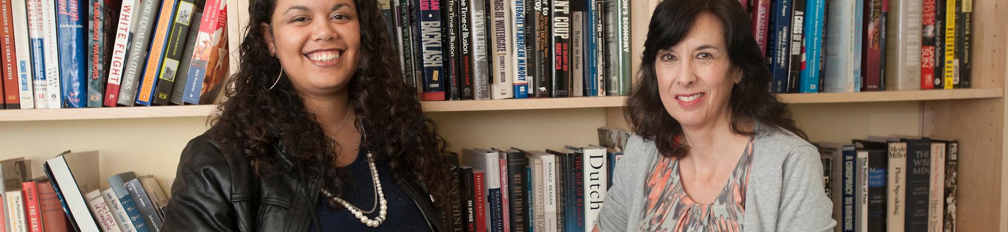 A PHD candidate and a History professor pose in front of a book shelf.