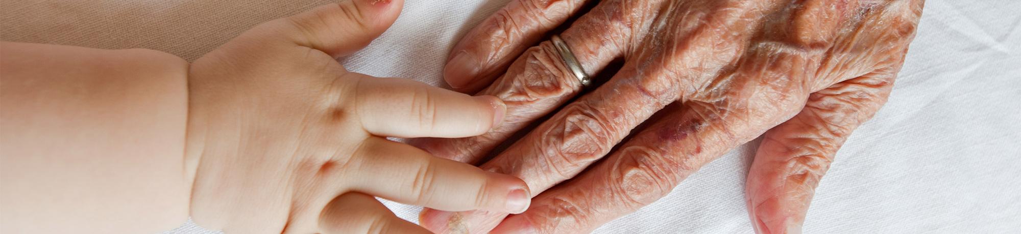 an infants hand touching an elderly persons hand