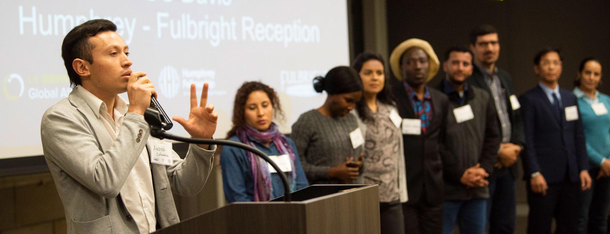 a student speaking at a podium and a group of students on stage