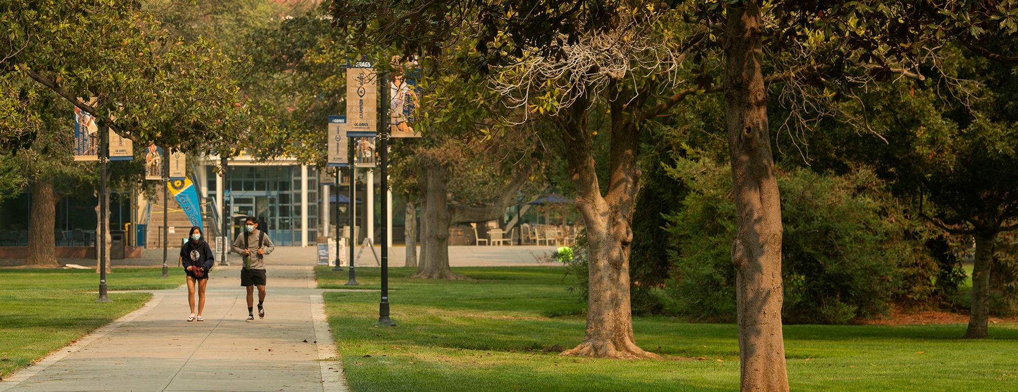 two students with masks walking through the quad
