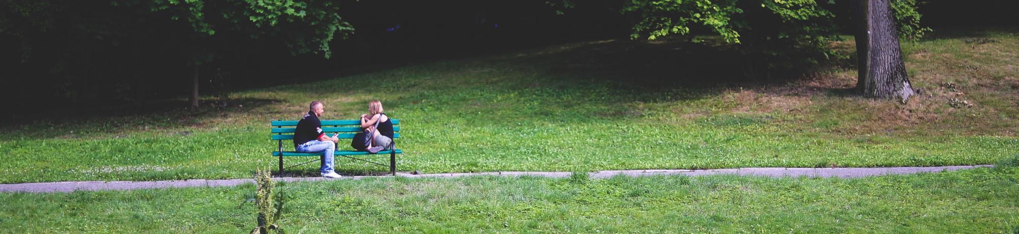 two people talking on a bench in a park