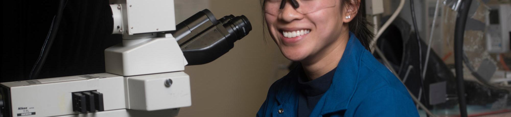 A female student smiling next to her microscope