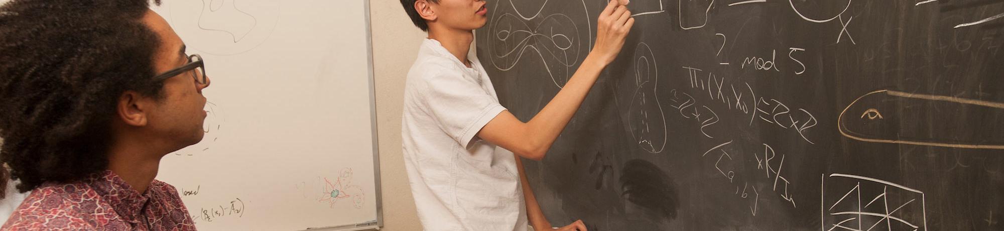 A student solves a complex equation on a blackboard