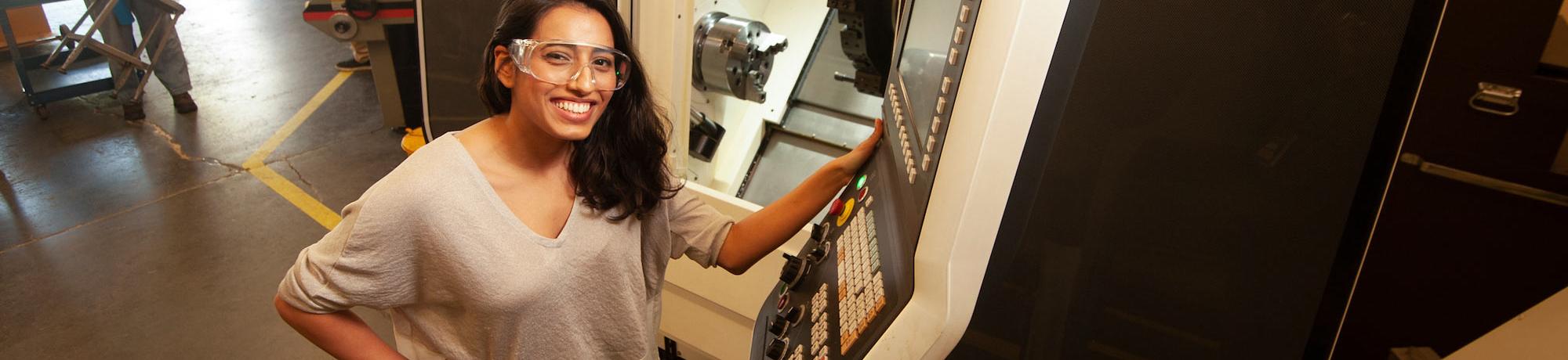 A female student in safety glasses exhibiting some machinery