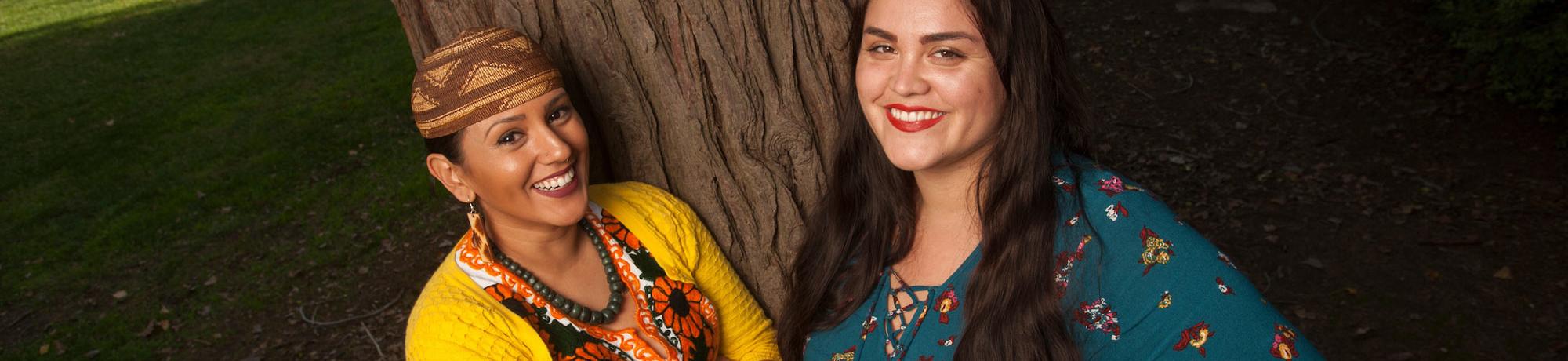 Two women pose in front of one of the oak trees on the UC Davis campus