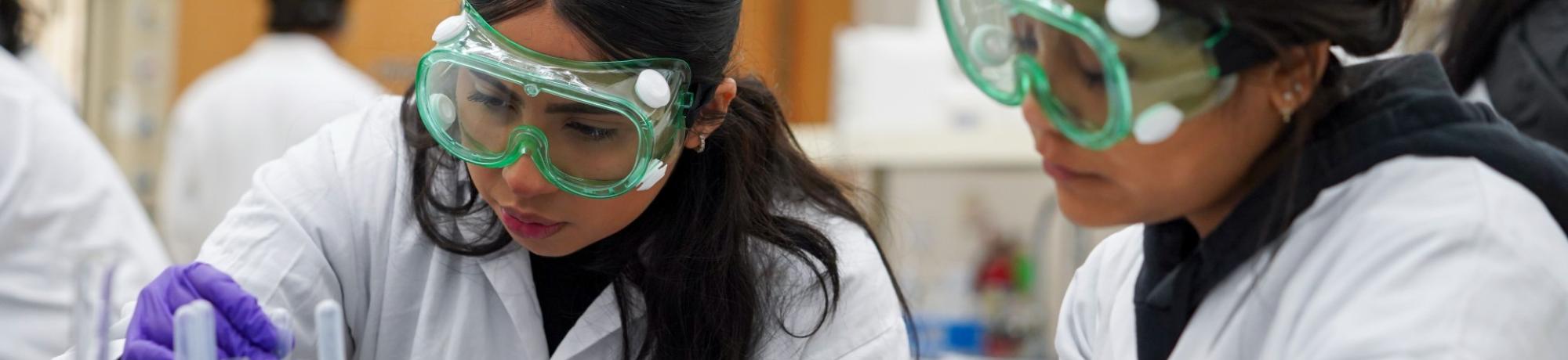 two chemistry tudent wear goggles at a lab bench while dealing with pharmaceuticals at UC Davis