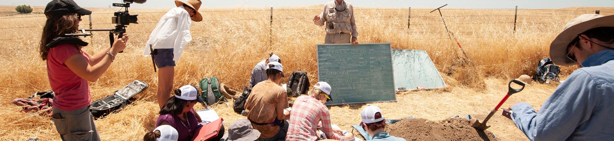 a professor conducting a soil science class with students outside