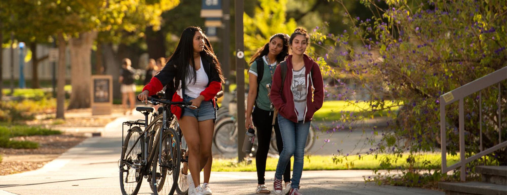 two students walking another another walking a bike near the quad
