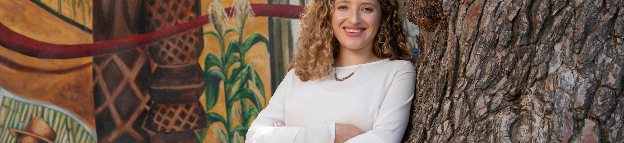 A female student poses in front of a mural