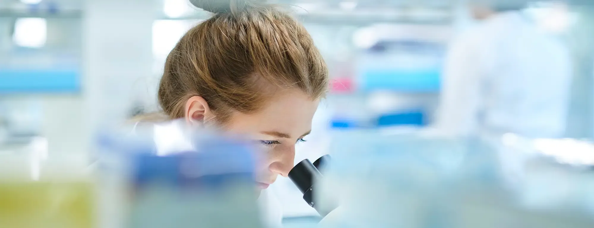 Young researcher peering into microscope in bright white laboratory photo