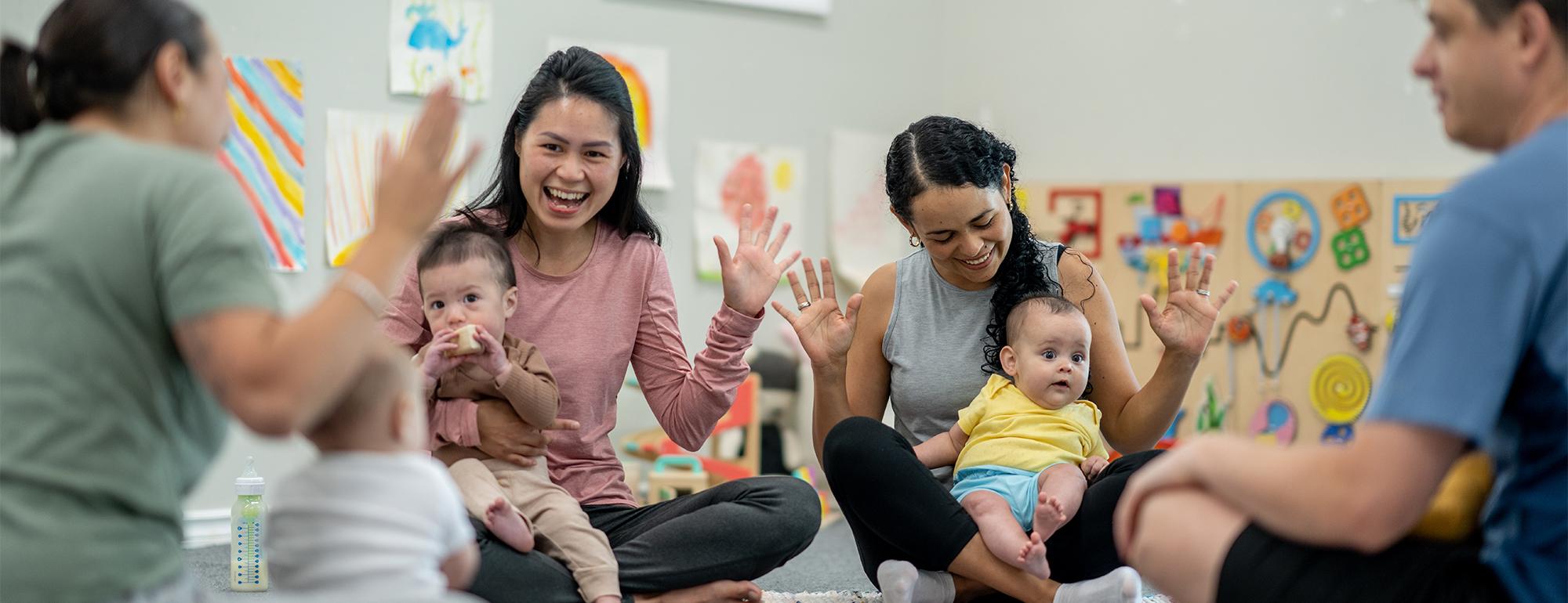 Parents and caregivers sitting in a circle smiling, holding babies in colorful classroom
