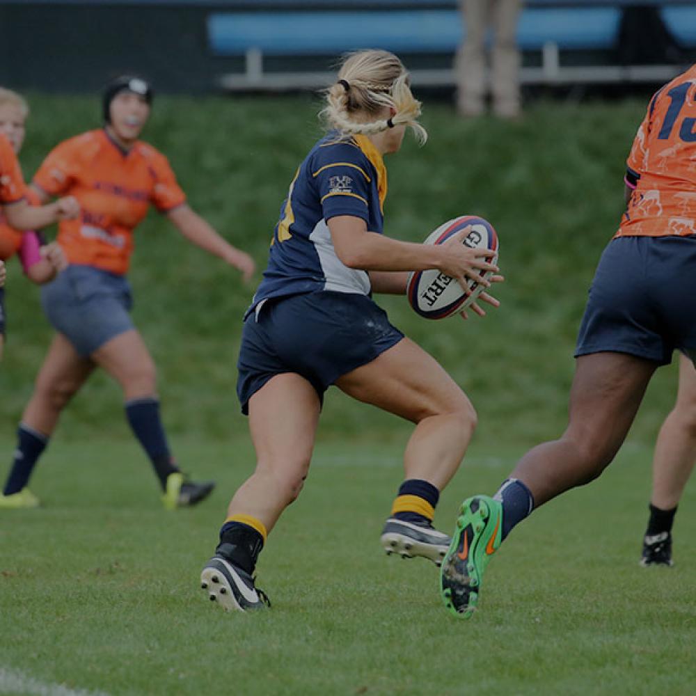 A women's rugby player charges down the field