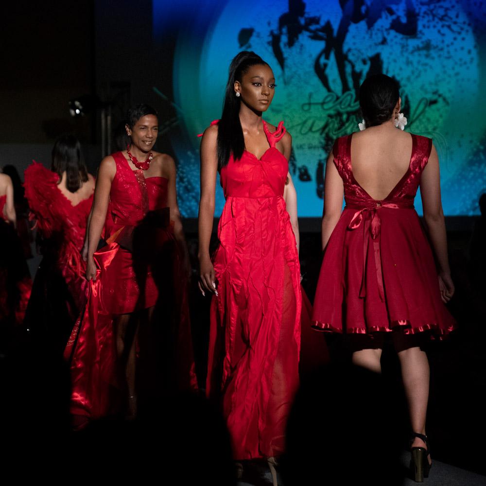 People in red dresses walking down a fashion runway at Picnic Day