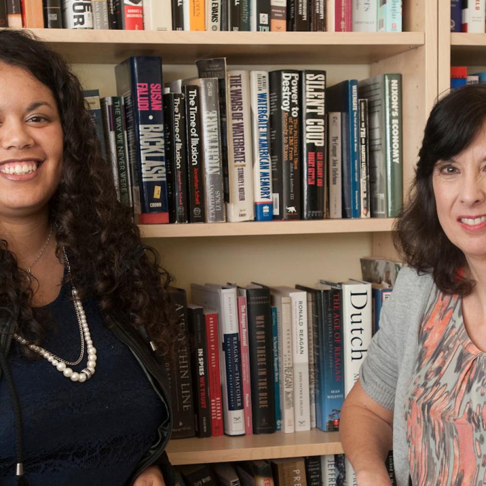 A PHD candidate and a History professor pose in front of a book shelf.