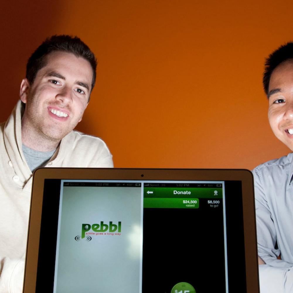 Two Graduate students pose with a laptop that shows the app that they created.