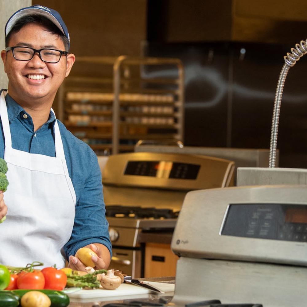 A male student poses with fruits and veggies in the research kitchen