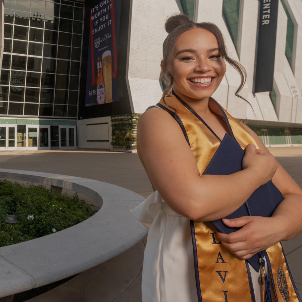 A UC Davis student standing outside of the Golden 1 center holdint their grad regalia