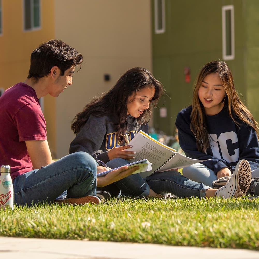 three freshman sitting on the grass in front of the residence halls