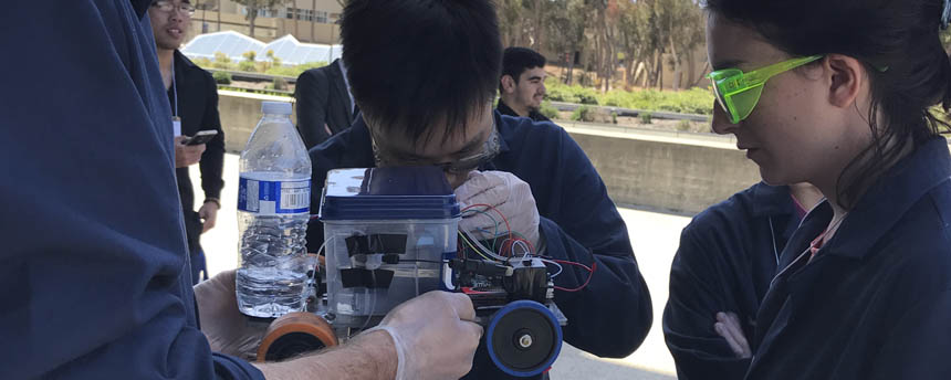 Two students closely examine wires around a miniature car