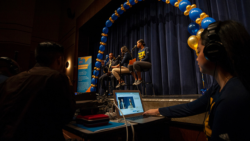 A femaie students at the controls for the podcast with interview on stage in front of her 