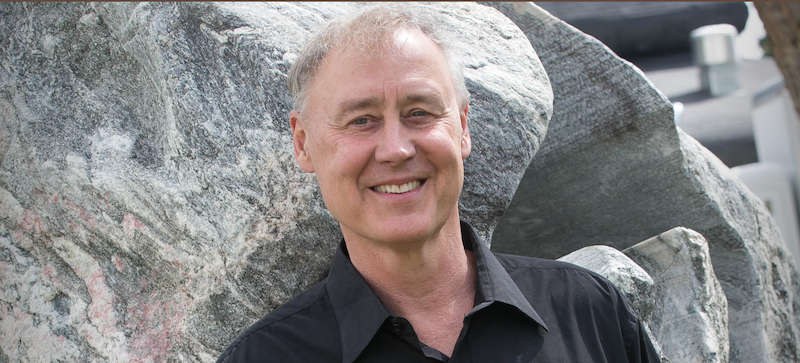Bruce Hornsby outside standing in front of large rocks.