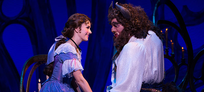 Belle and the Beast facing each other, smiling and holding hands.