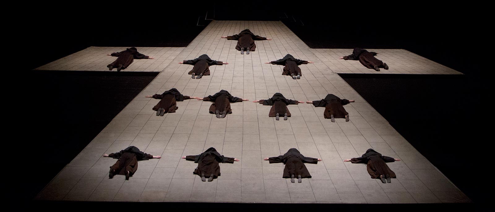 Nuns lying prostrate in the formation of a crucifix, with their arms extended out to their sides,