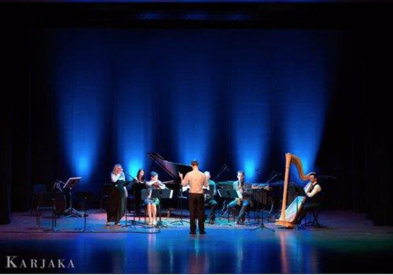 Members of the ensemble performing on stage in front of a dramatically lit blue background.