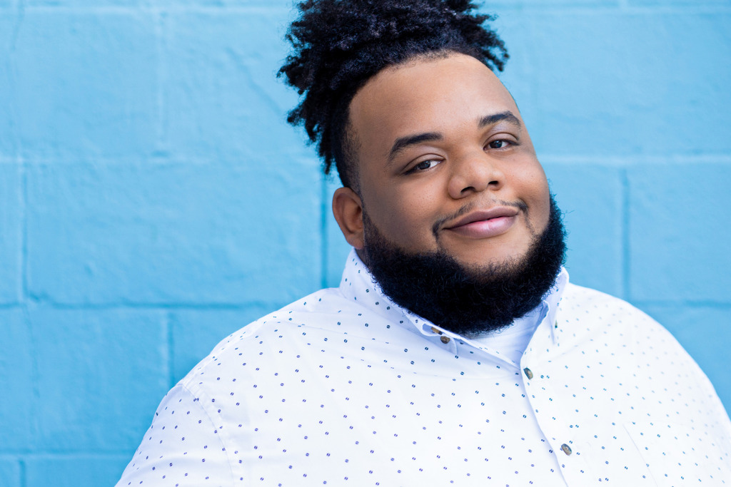 A photo of Kiry Shabazz standing in front of a blue background.