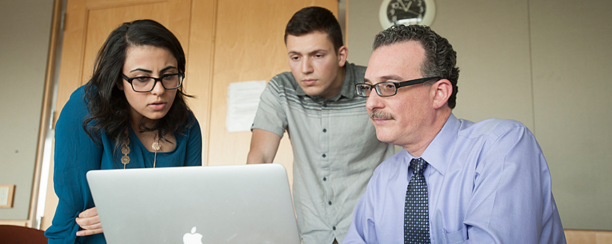 Male professor at computer with woman and young male listening to him