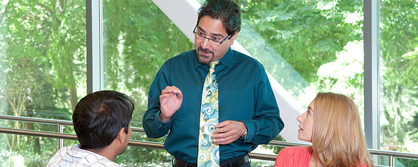 Man in tie standing and talking to two seated students