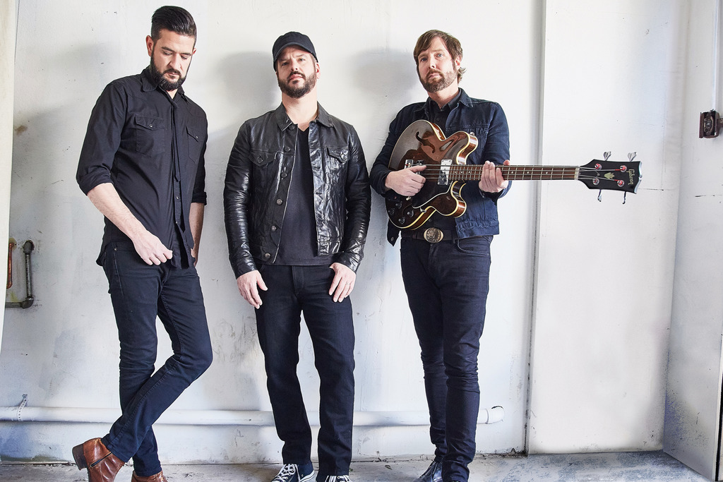 The three members of the band, one of them holding a guitar.