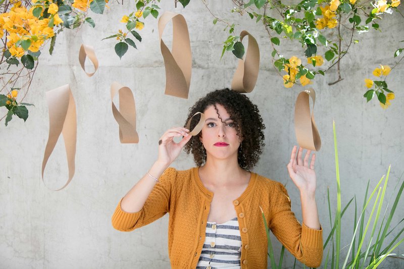 Sumaia Jackson standing in front a cement wall with flowers above her.